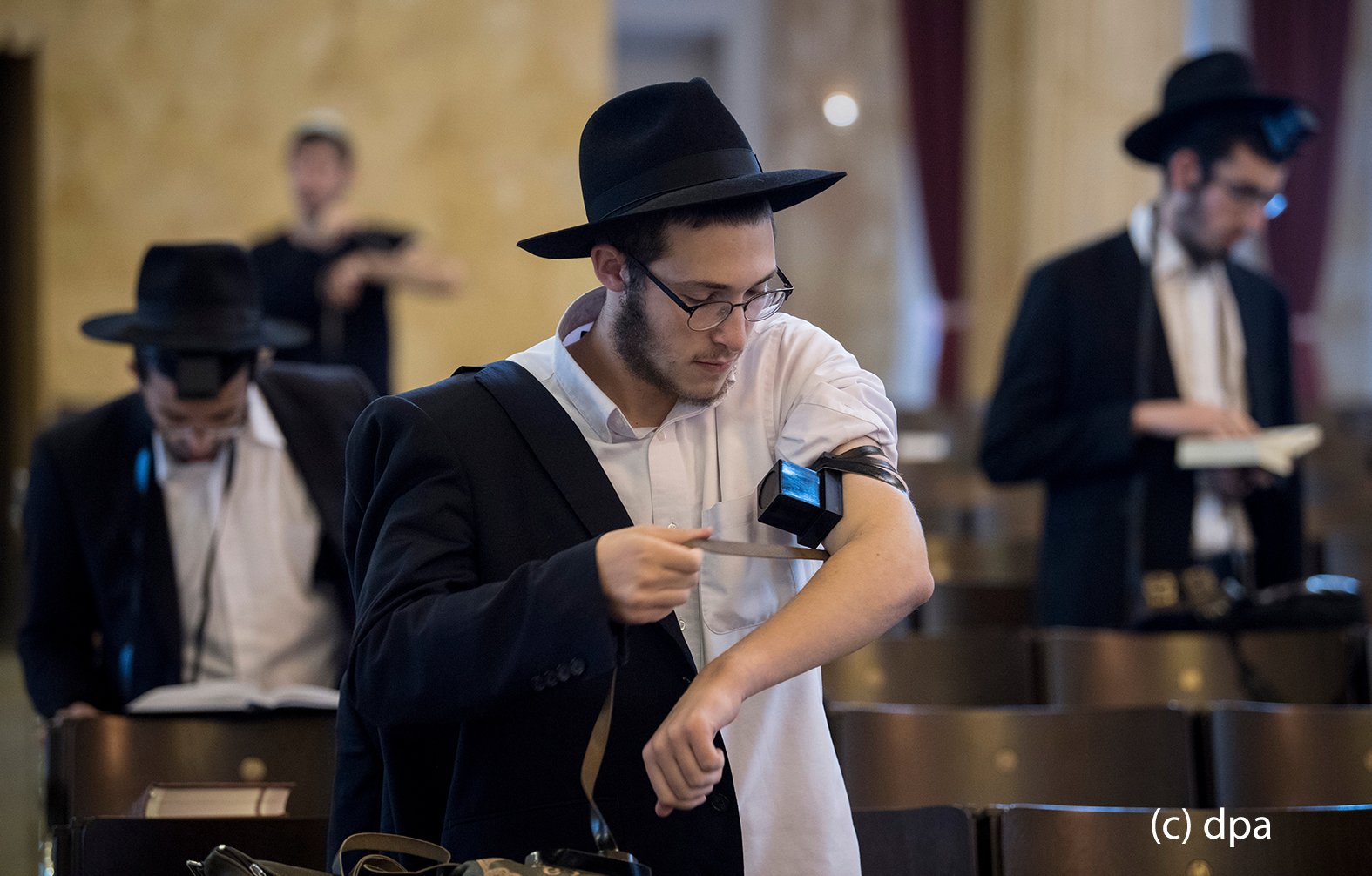 Zur weiteren Vorbereitung des Gebetes legt sich ein gläubiger Jude in der Westend-Synagoge in Frankfurt am Main einen Gebetsriemen aus Leder an. Zu dem Riemen gehören auch zwei "Kästchen", von denen eins am Oberarm ("In der Nähe des Herzens") und ein weiteres an der Stirn ("In er Nähe des Verstandes") plaziert wird. In der Synagoge kommen die Gläubigen aus unterschiedlichen Glaubensausrichtungen bis zu dreimal täglich zum Gebet zusammen. 