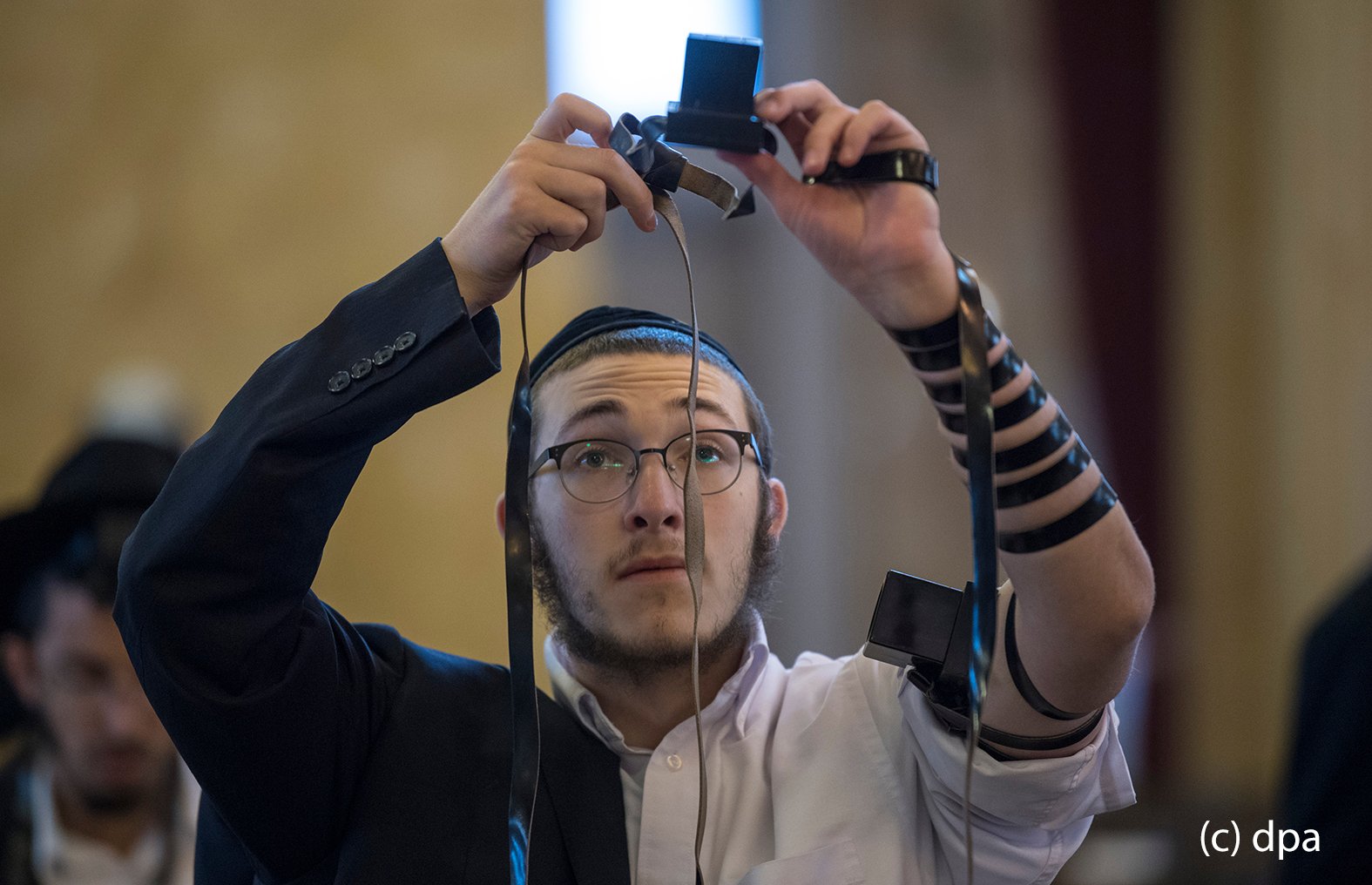 Zur weiteren Vorbereitung des Gebetes legt sich ein gläubiger Jude in der Westend-Synagoge in Frankfurt am Main einen Gebetsriemen aus Leder an. Zu dem Riemen gehören auch zwei "Kästchen", von denen eins am Oberarm ("In der Nähe des Herzens") und ein weiteres an der Stirn ("In er Nähe des Verstandes") plaziert wird. In der Synagoge kommen die Gläubigen aus unterschiedlichen Glaubensausrichtungen bis zu dreimal täglich zum Gebet zusammen. 