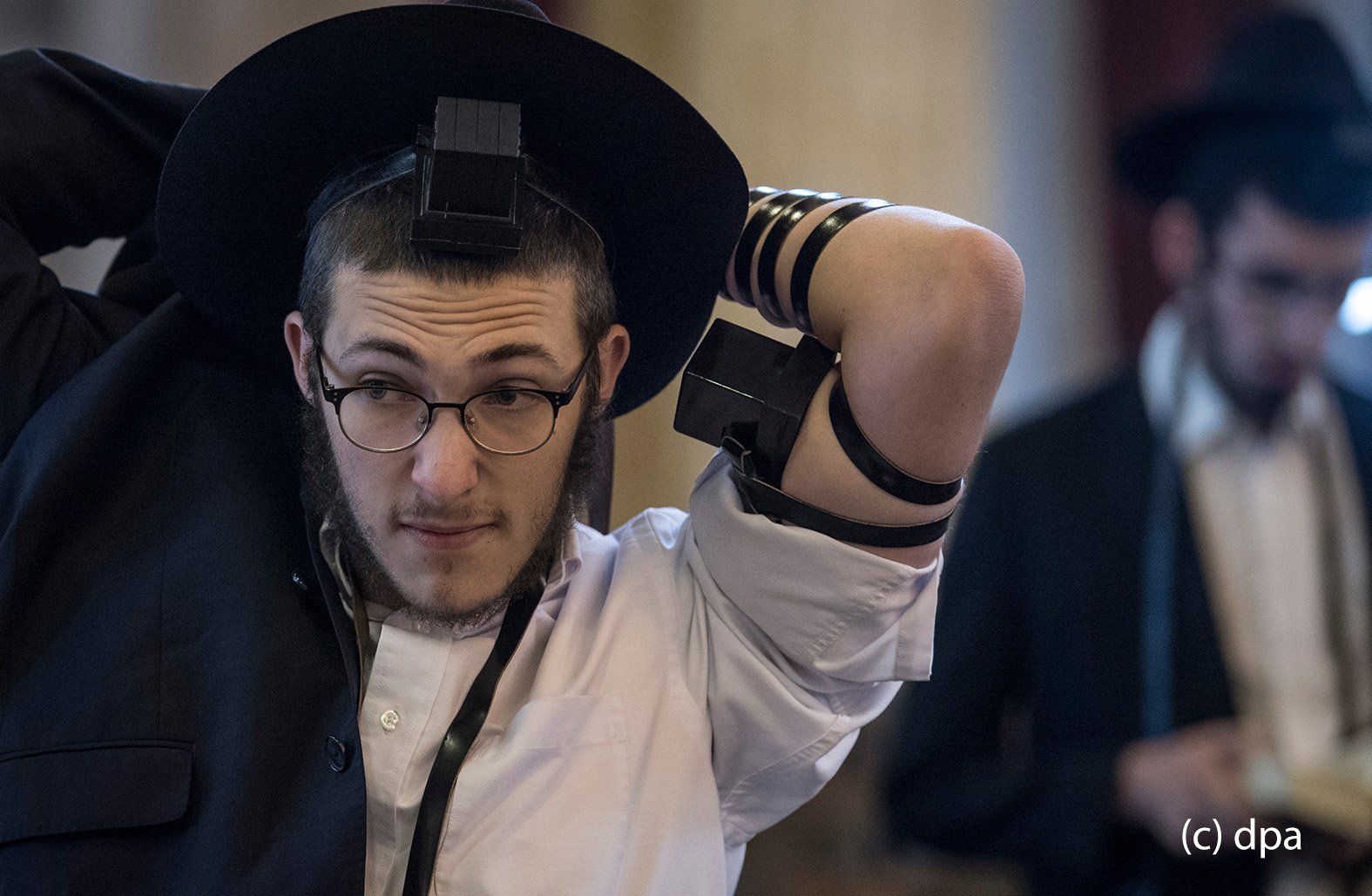 Zur weiteren Vorbereitung des Gebetes legt sich ein gläubiger Jude in der Westend-Synagoge in Frankfurt am Main einen Gebetsriemen aus Leder an. Zu dem Riemen gehören auch zwei "Kästchen", von denen eins am Oberarm ("In der Nähe des Herzens") und ein weiteres an der Stirn ("In er Nähe des Verstandes") plaziert wird. In der Synagoge kommen die Gläubigen aus unterschiedlichen Glaubensausrichtungen bis zu dreimal täglich zum Gebet zusammen. 